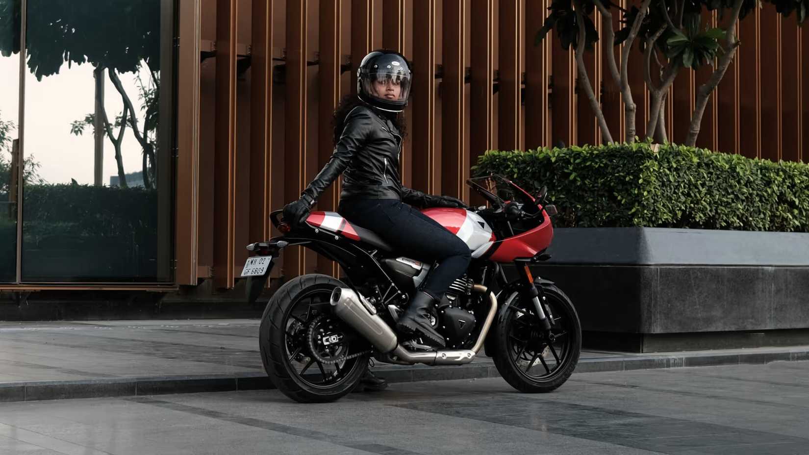 Piloto olhando por cima do ombro montado em uma Triumph Thruxton 400 em frente a uma parede