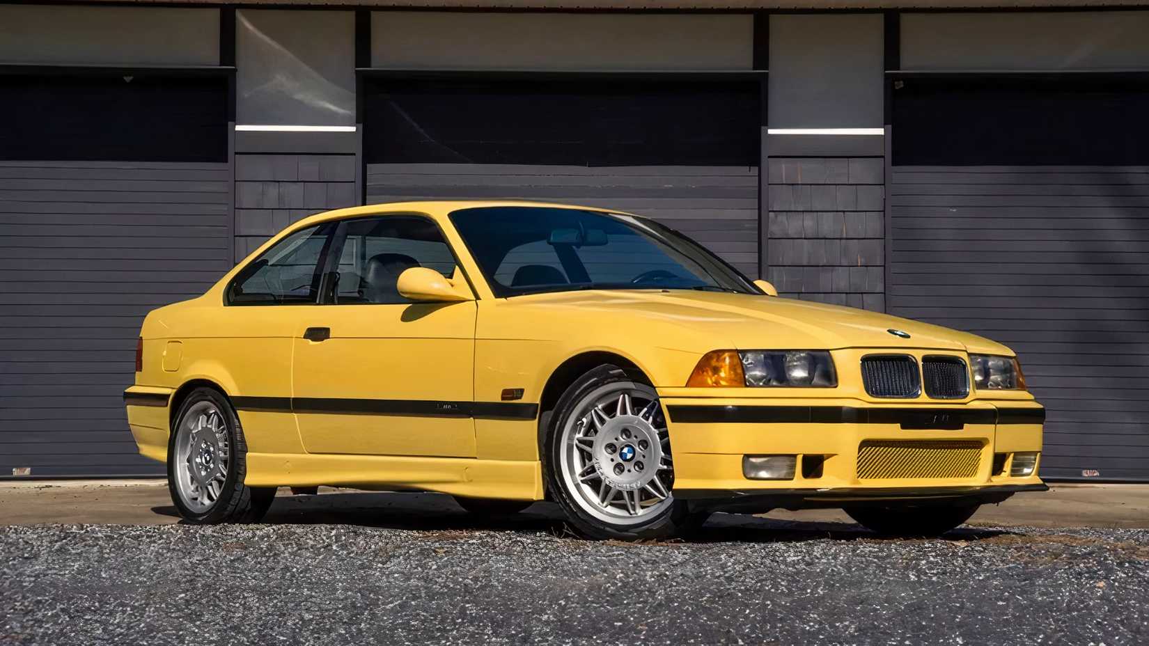 Foto frontal 3/4 de um BMW M3 1995 em amarelo estacionado em frente à garagem
