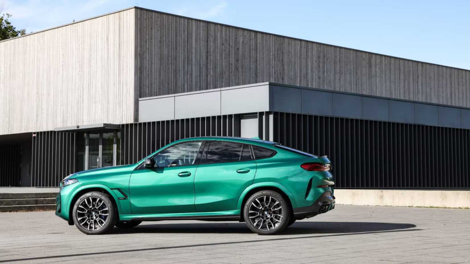 A side-profile shot of a green 2026 BMW X6 M60i parked in front of building