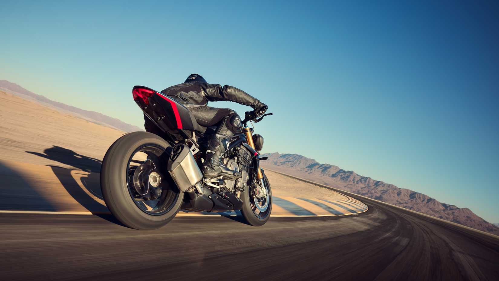 Foto de rastreamento em ângulo baixo da traseira da Triumph Speed Triple 1200 RS passando por uma curva em uma pista de corrida