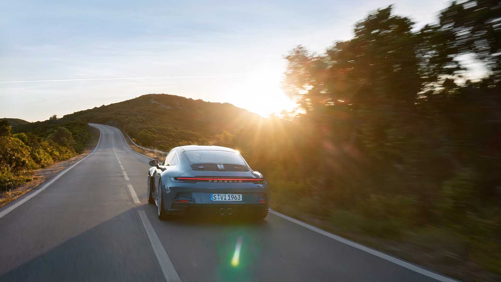 Vista traseira de um Porsche 911 S/T 2024 dirigindo em uma estrada ao pôr do sol.
