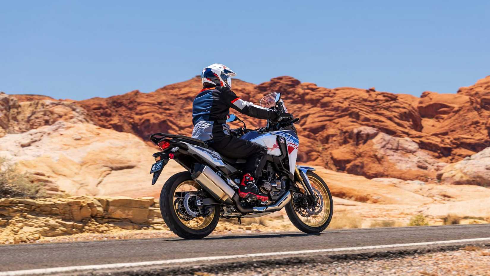 Foto de uma Honda Africa Twin Adventure Sports ES 2026 andando na estrada em frente a um terreno desértico