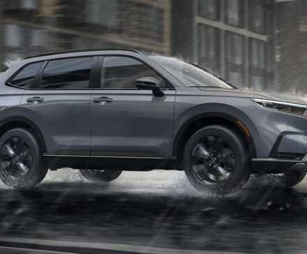 Foto de perfil lateral de um Honda CR-V Sport Touring Hybrid cinza 2026 dirigindo na chuva.