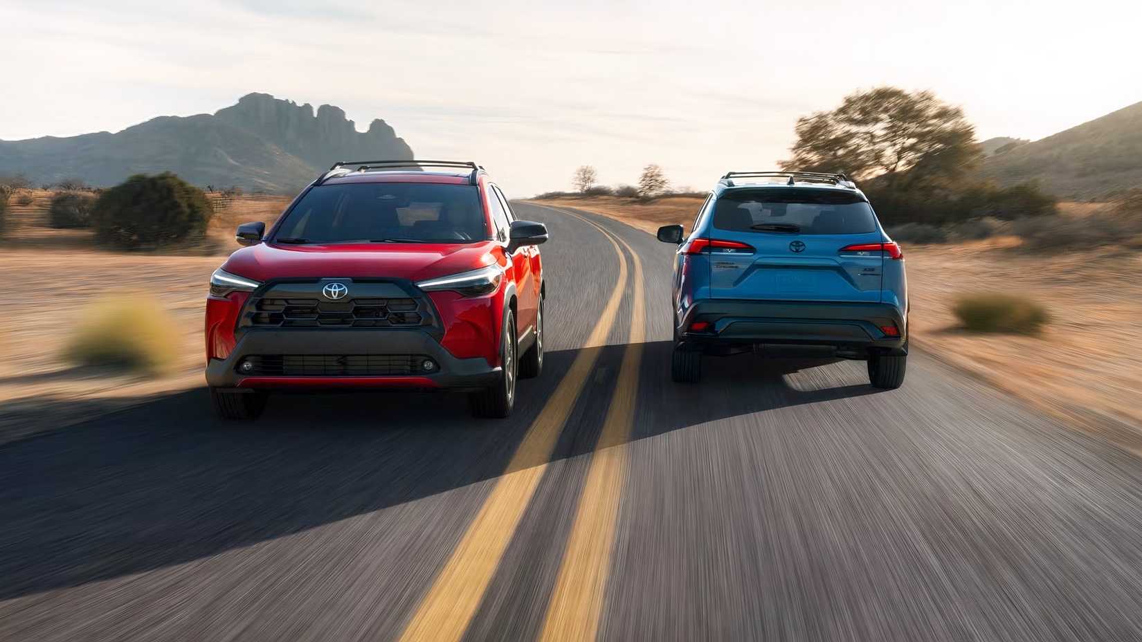 2026 Toyota Corolla Cross blue hybrid model and red regular model driving in opposite directions on a road