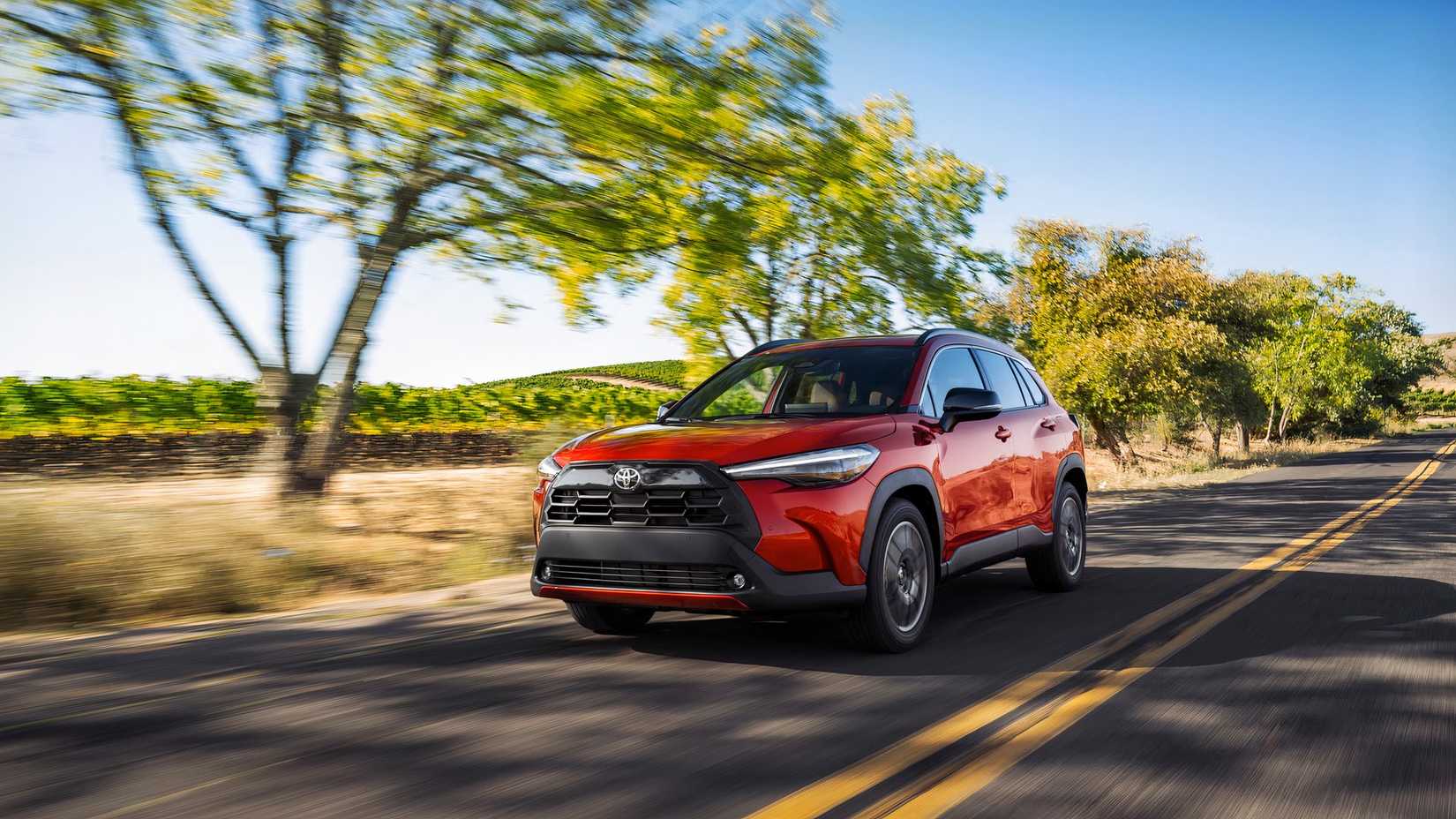 Foto frontal de um Toyota Corolla Cross 2026 vermelho dirigindo por uma estrada secundária