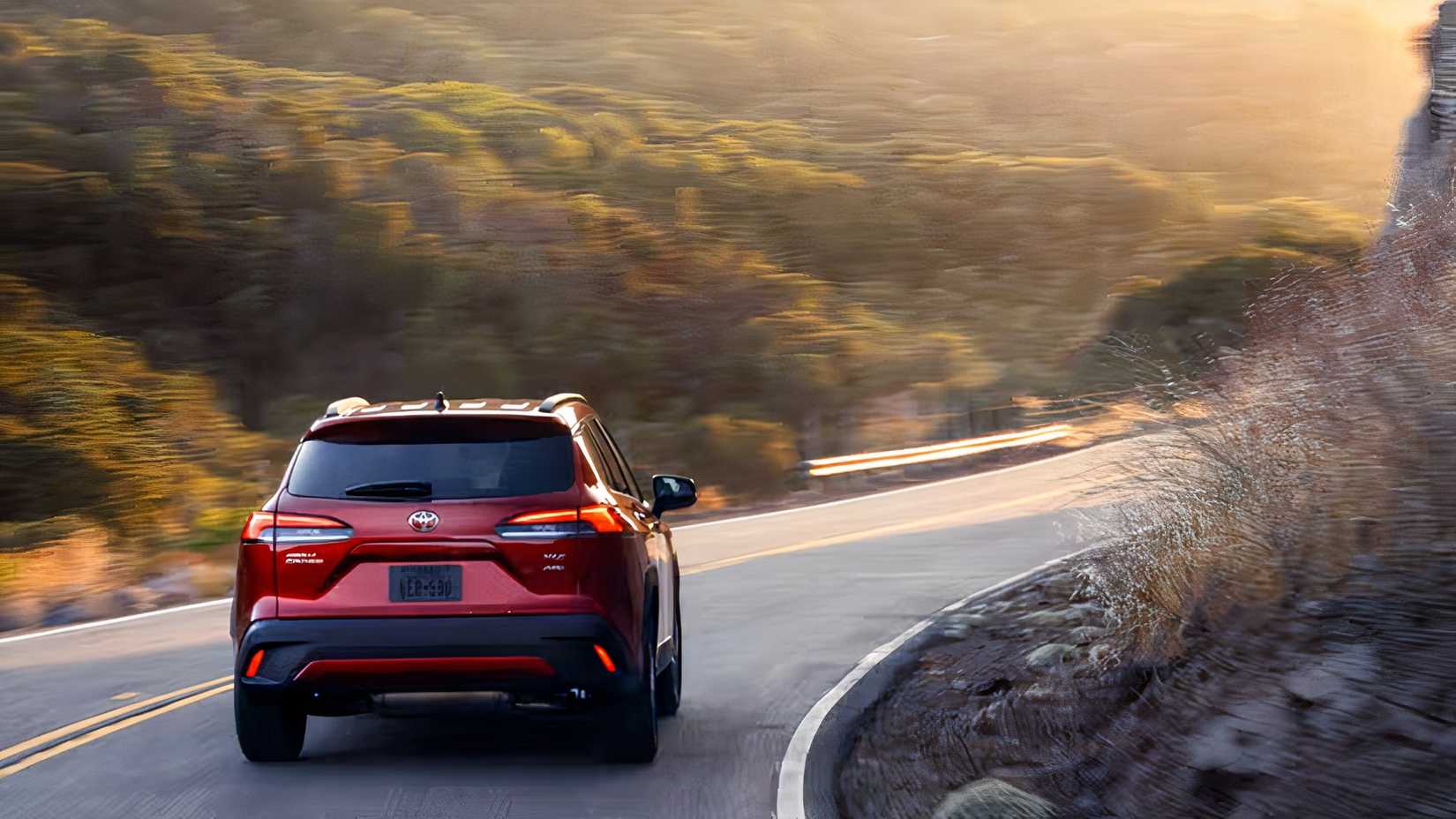 Rear shot of a red 2026 Toyota Corolla Cross driving down winding road