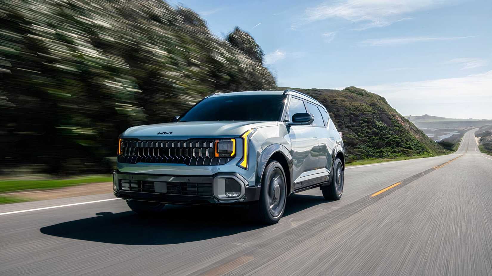 Foto frontal de um Kia Seltos Hybrid 2027 azul dirigindo por uma estrada panorâmica