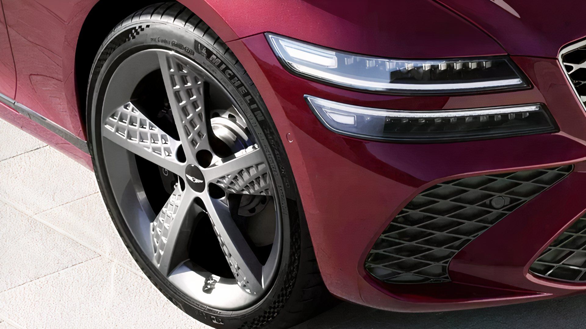 Front-end close-up shot of a red 2026 Genesis G80's front wheel and headlight