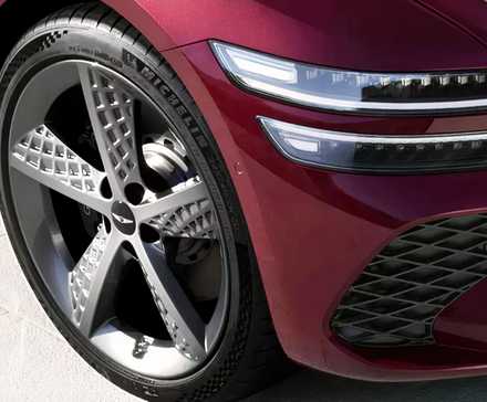 Front-end close-up shot of a red 2026 Genesis G80's front wheel and headlight