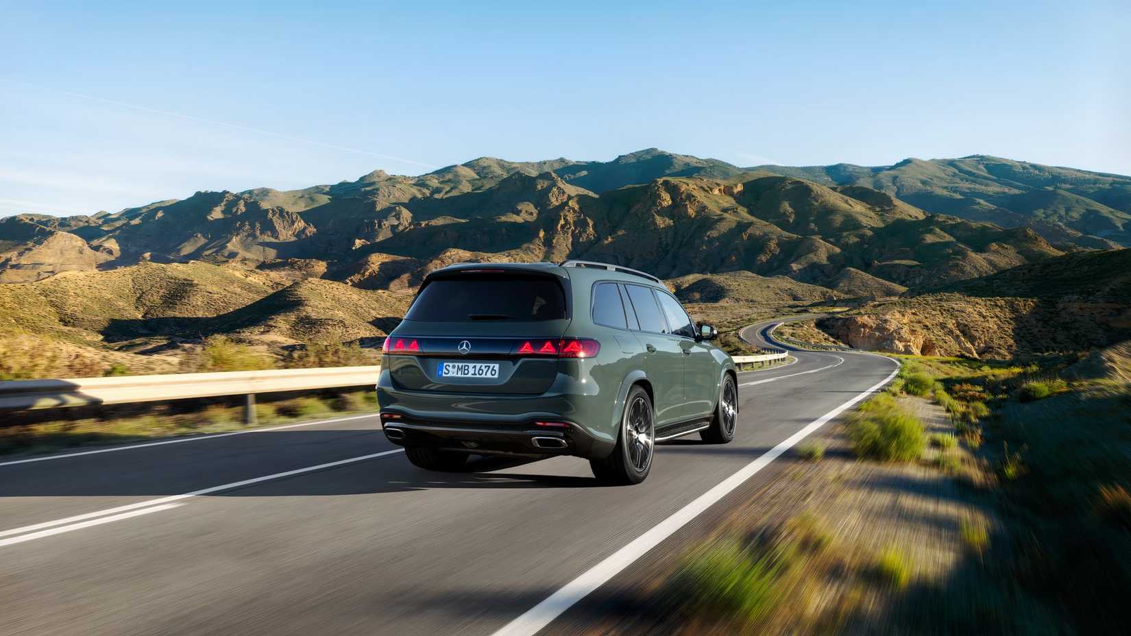 Foto traseira 3/4 de um Mercedes-Benz GLS 2027 verde descendo uma estrada de montanha
