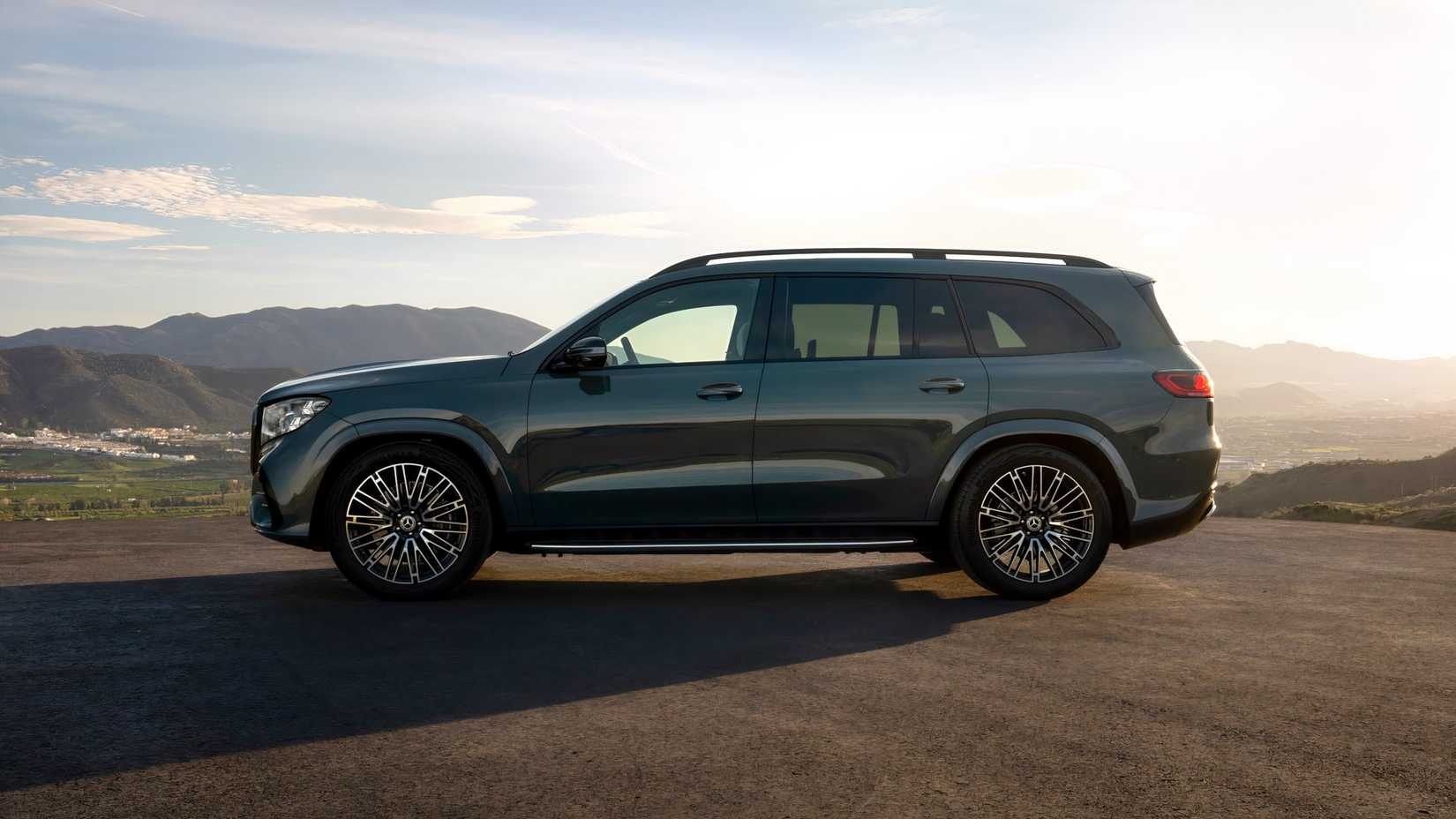 Fotografia lateral de um Mercedes-Benz GLS 2027 verde estacionado em frente a montanhas