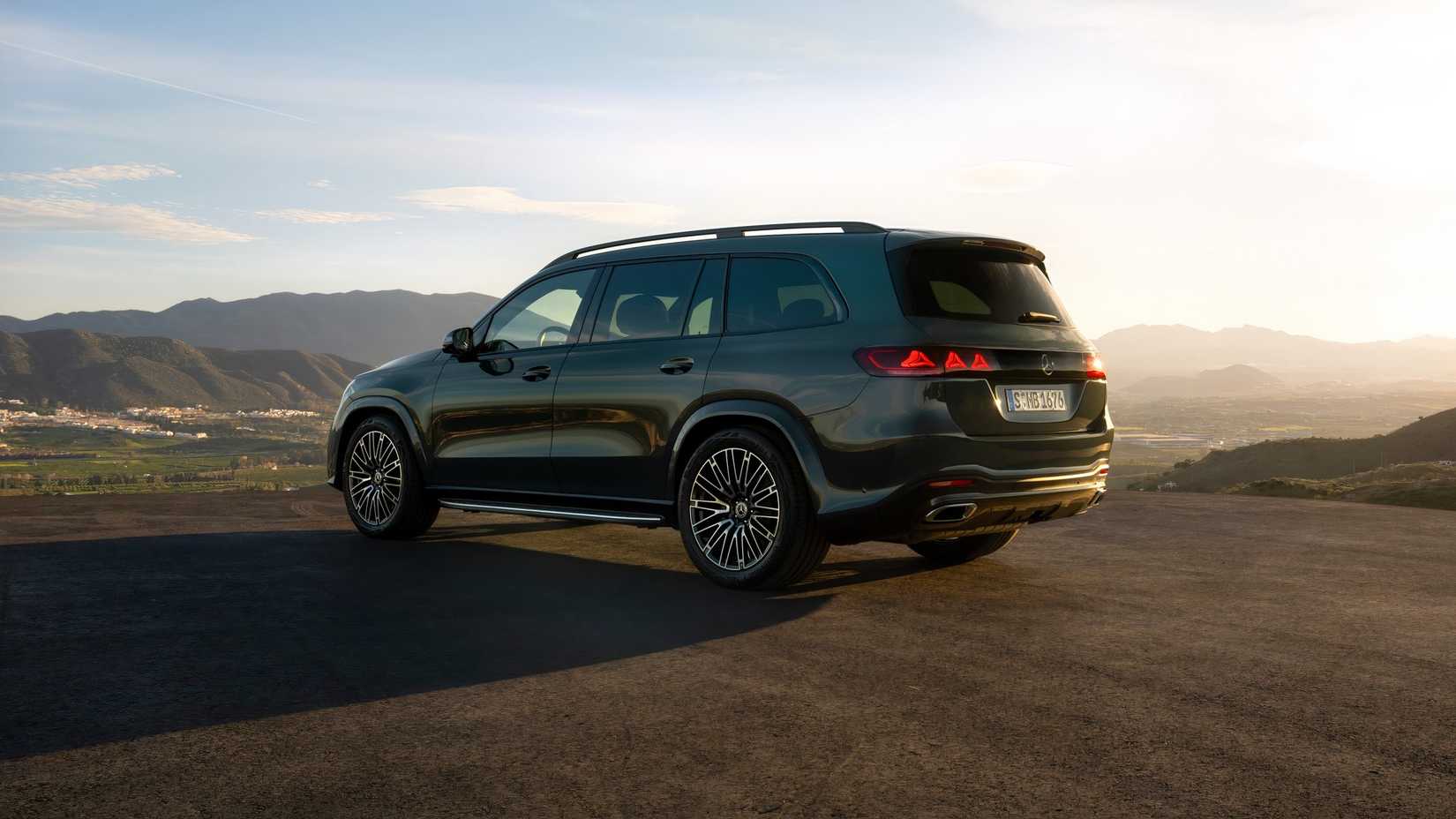 Foto traseira 3/4 de um Mercedes-Benz GLS 2027 verde estacionado em frente a montanhas