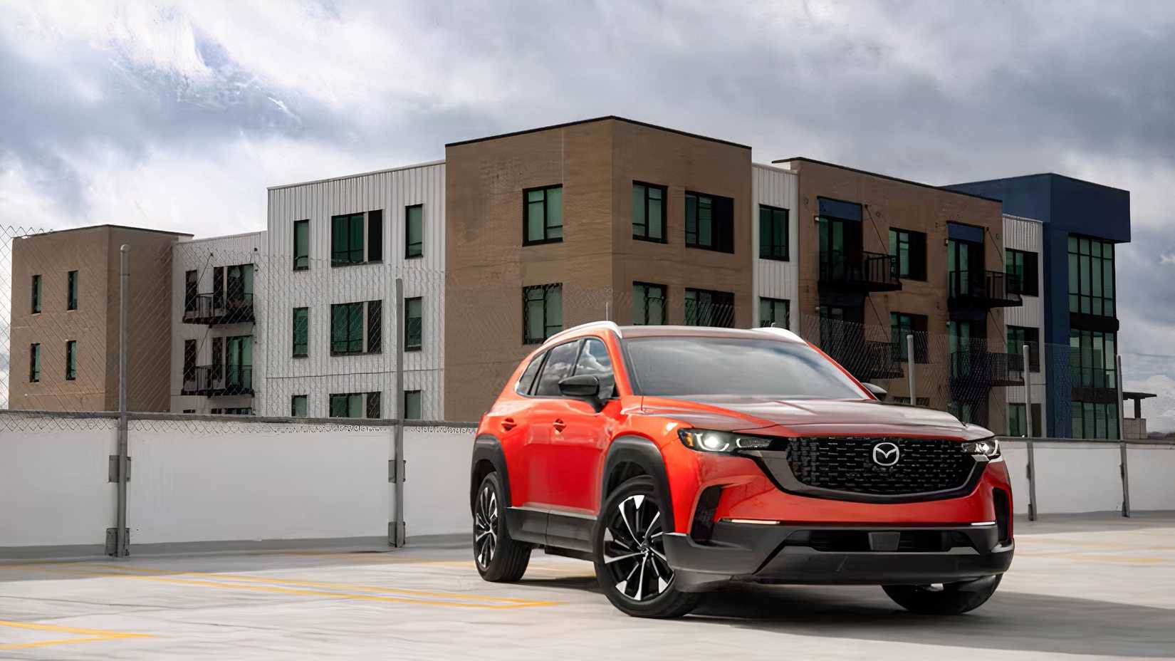 Front 3/4 shot of an orange 2026 Mazda CX-50 Hybrid parked in front of houses