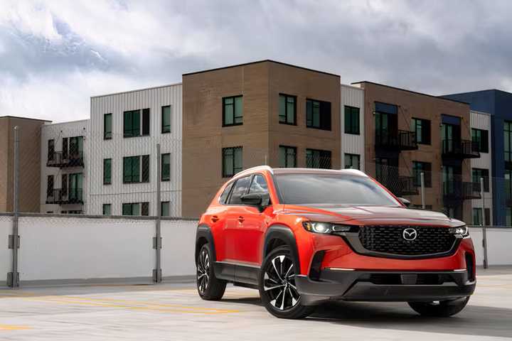 Foto frontal 3/4 de um Mazda CX-50 Hybrid 2026 laranja estacionado em frente a casas