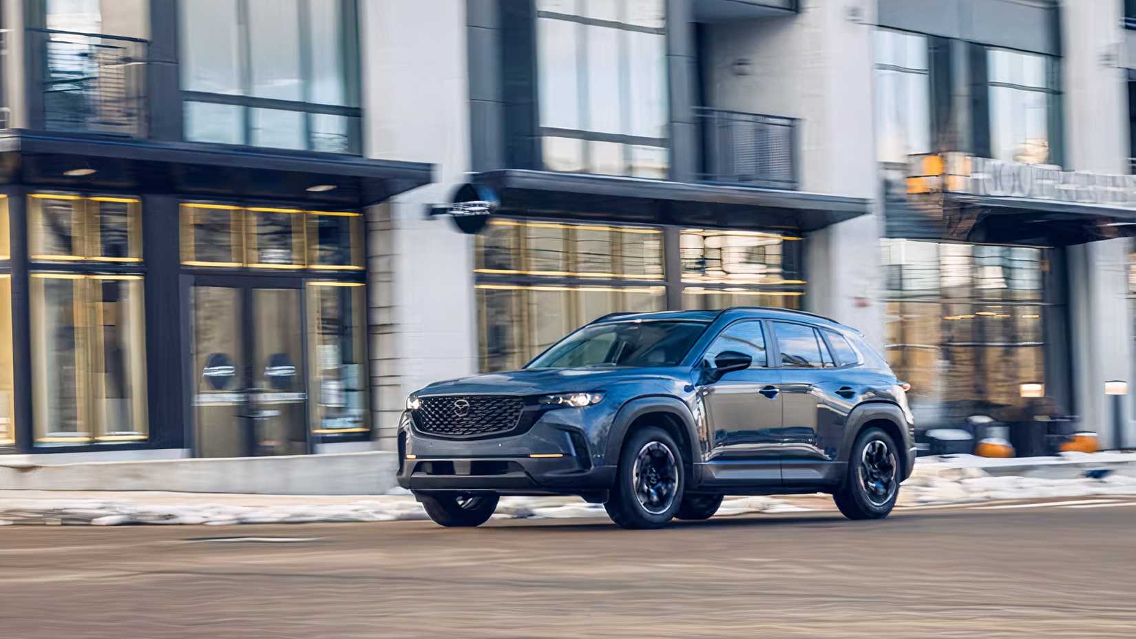 Front 3/4 shot of a blue 2026 Mazda CX-50 driving through city