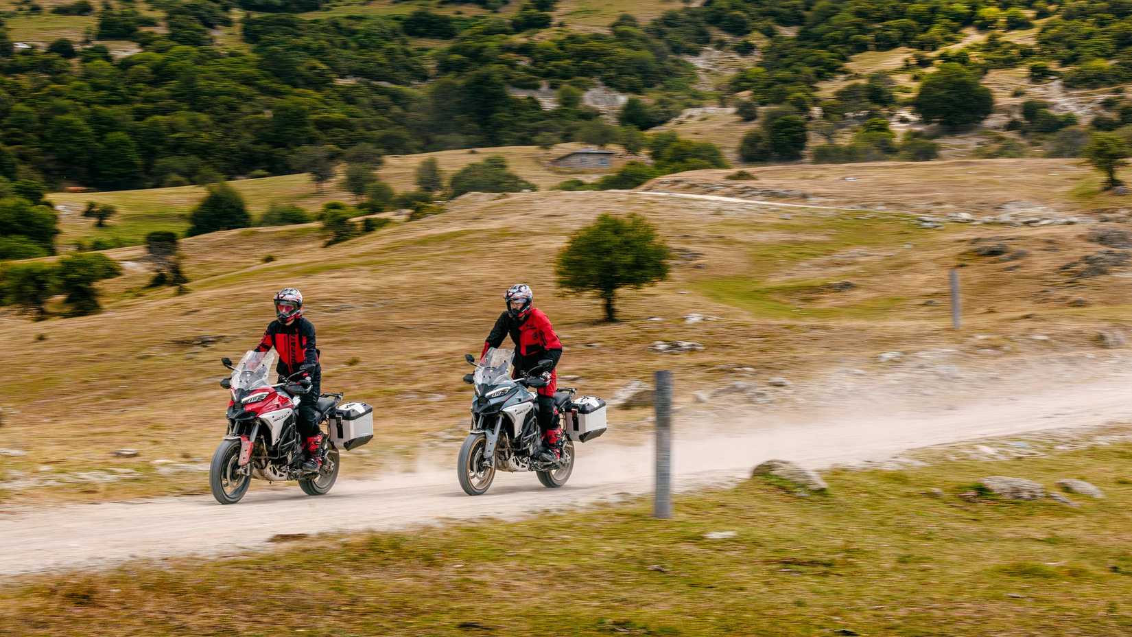 Dois pilotos na Ducati Multistrada V4 Rallys em pé e andando por uma estrada de terra