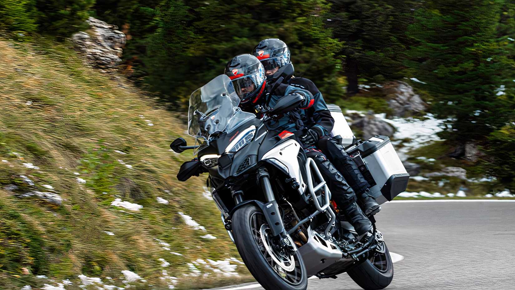 Rider and pillion on a Ducati Multistrada V4 Rally with snow dotting the background landscape