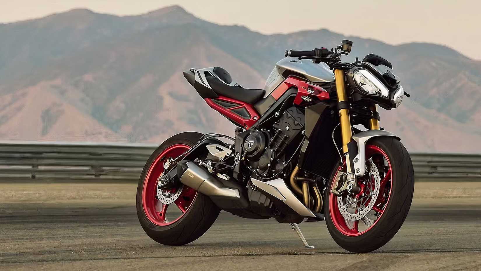 Triumph Street Triple 765 RX com detalhes em vermelho estacionada ao lado de uma pista de corrida com montanhas ao fundo