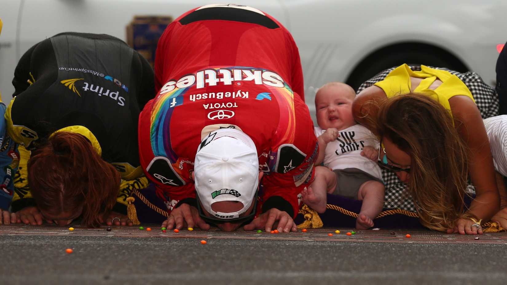 Kyle Busch, motorista do Skittles Toyota nº 18, comemora com sua esposa Samantha e seu filho Brexton beijando os tijolos após vencer a NASCAR Sprint Cup Series Crown Royal apresenta o Jeff Kyle 400 no Brickyard em Indianapolis Motor Speedway em 26 de julho de 2015 em Indianápolis, Indiana.