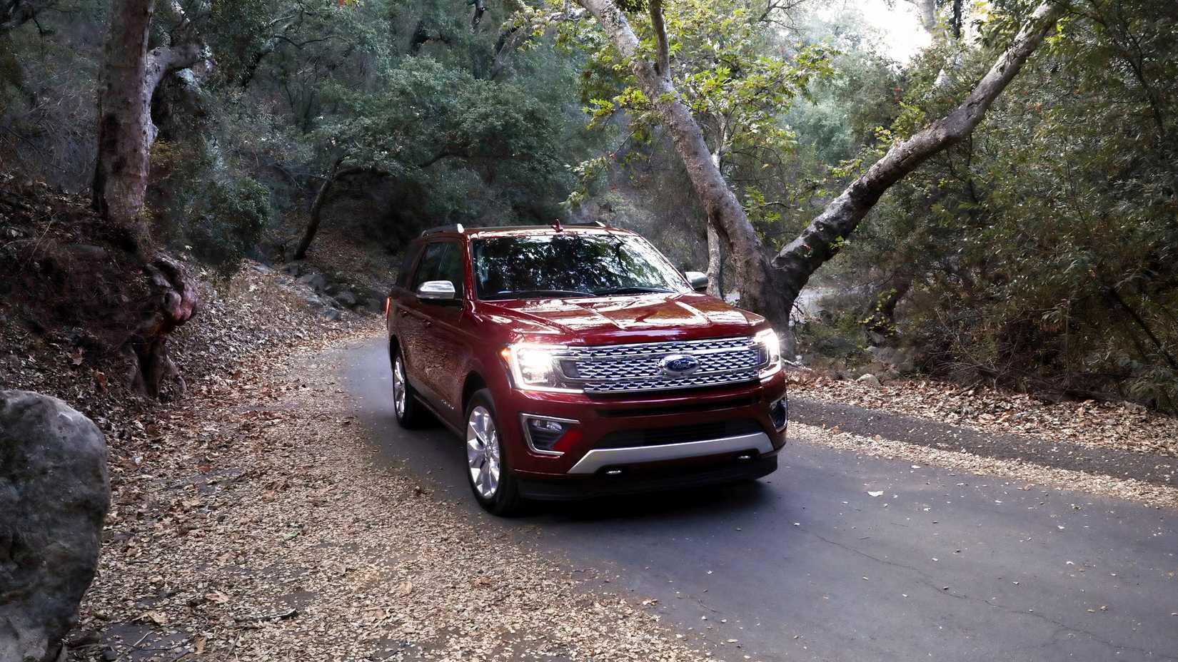 Foto frontal de uma Expedição Ford 2018 dirigindo por uma estrada arborizada