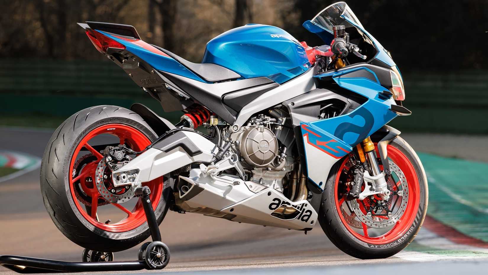 2026 Aprilia RS 660 estacionada em um suporte de paddock, vista traseira do terceiro quarto