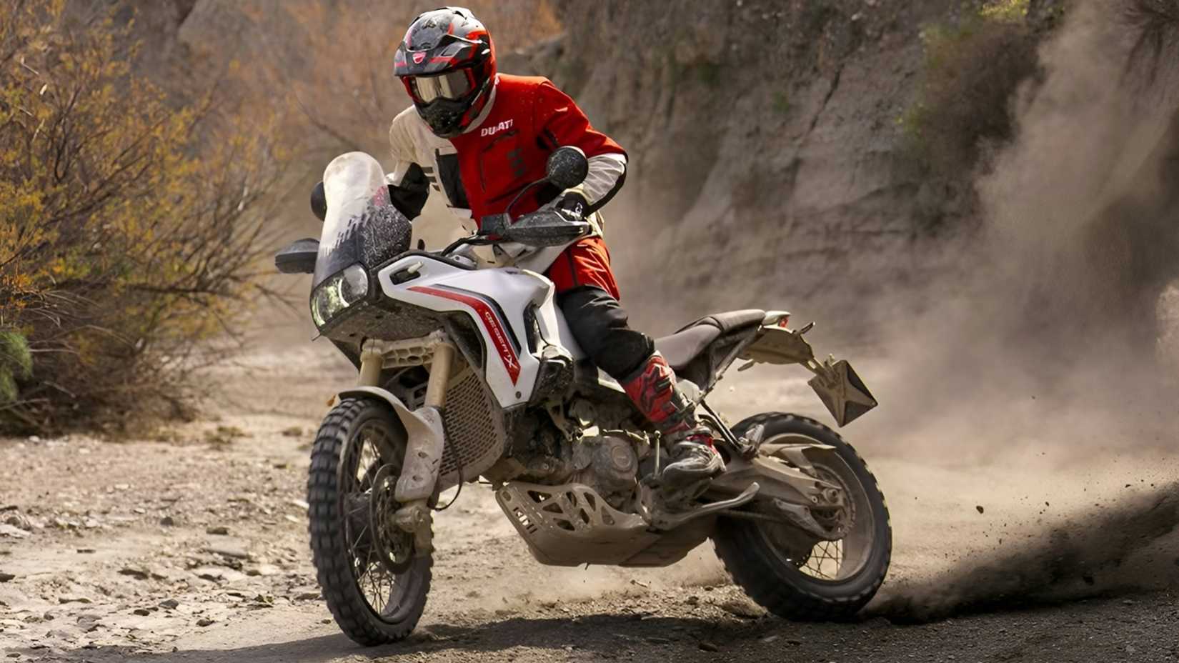 Ducati DesertX V2 sliding through the dirt in front of a cinematic shot of the third quarter