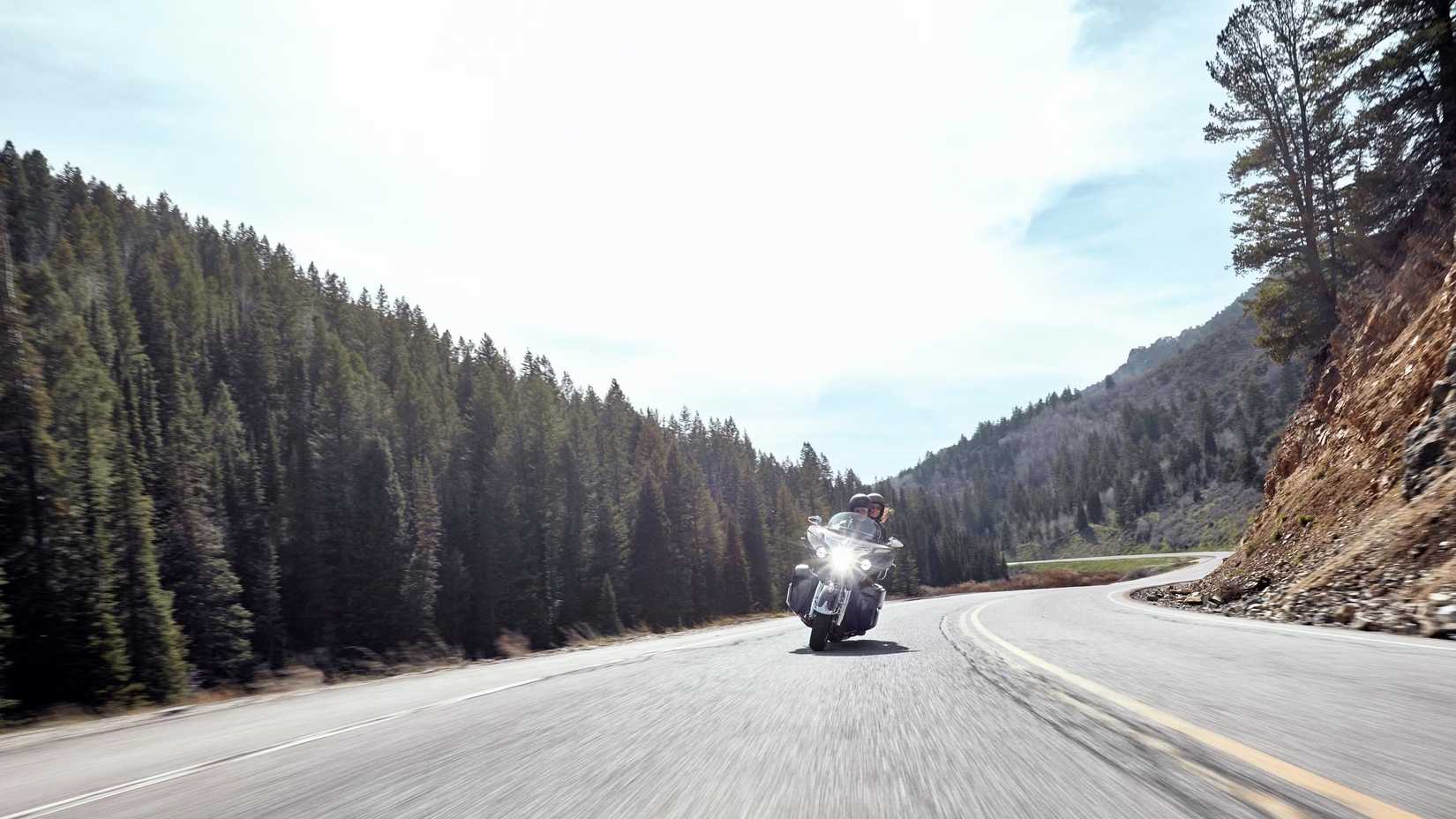 Indian Roadmaster fazendo curvas em uma curva acentuada em uma rodovia deserta com abetos de um lado e uma montanha do outro