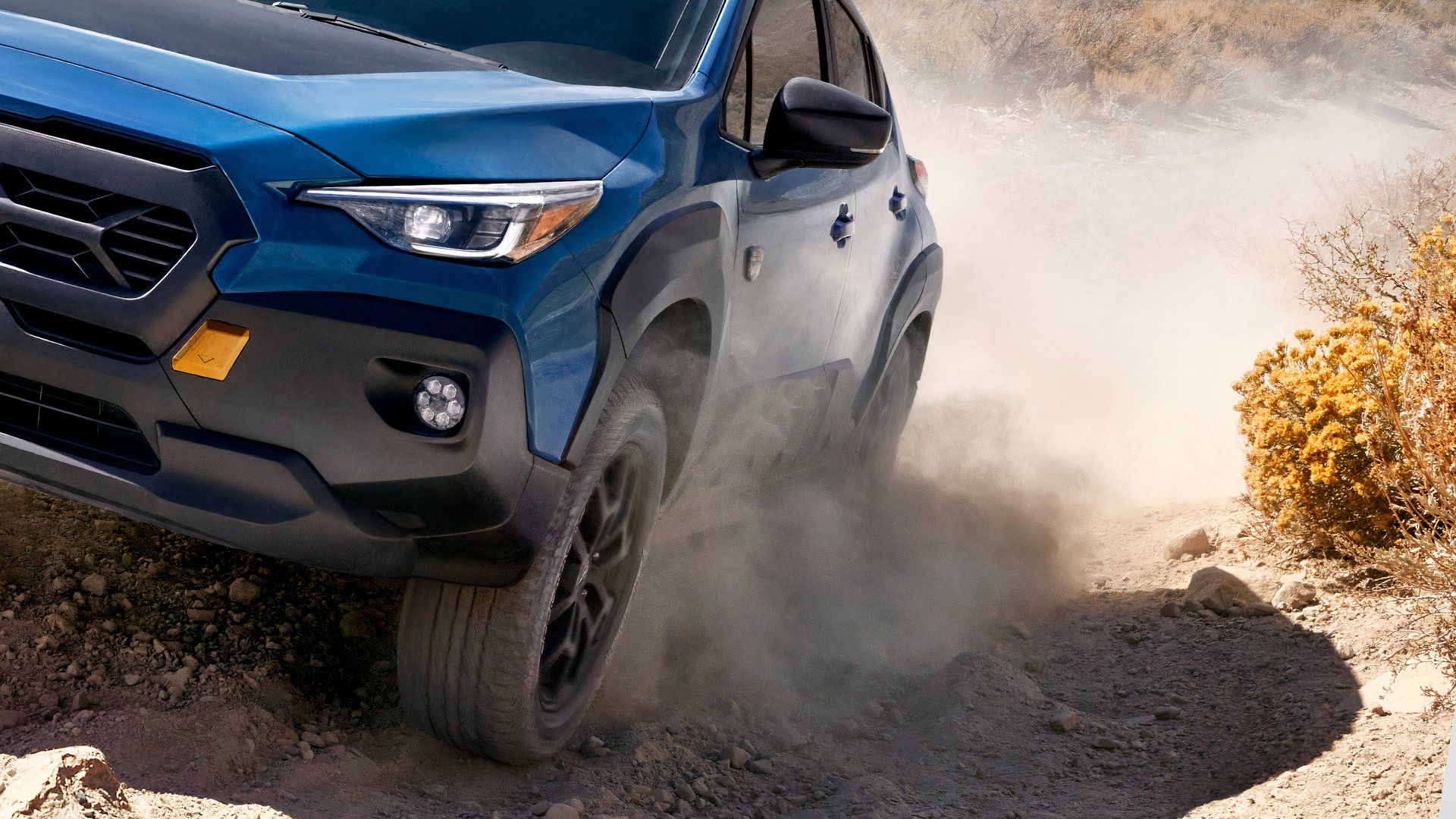 Close da frente de um Subaru Crosstrek Wilderness 2024 azul dirigindo em uma trilha rochosa