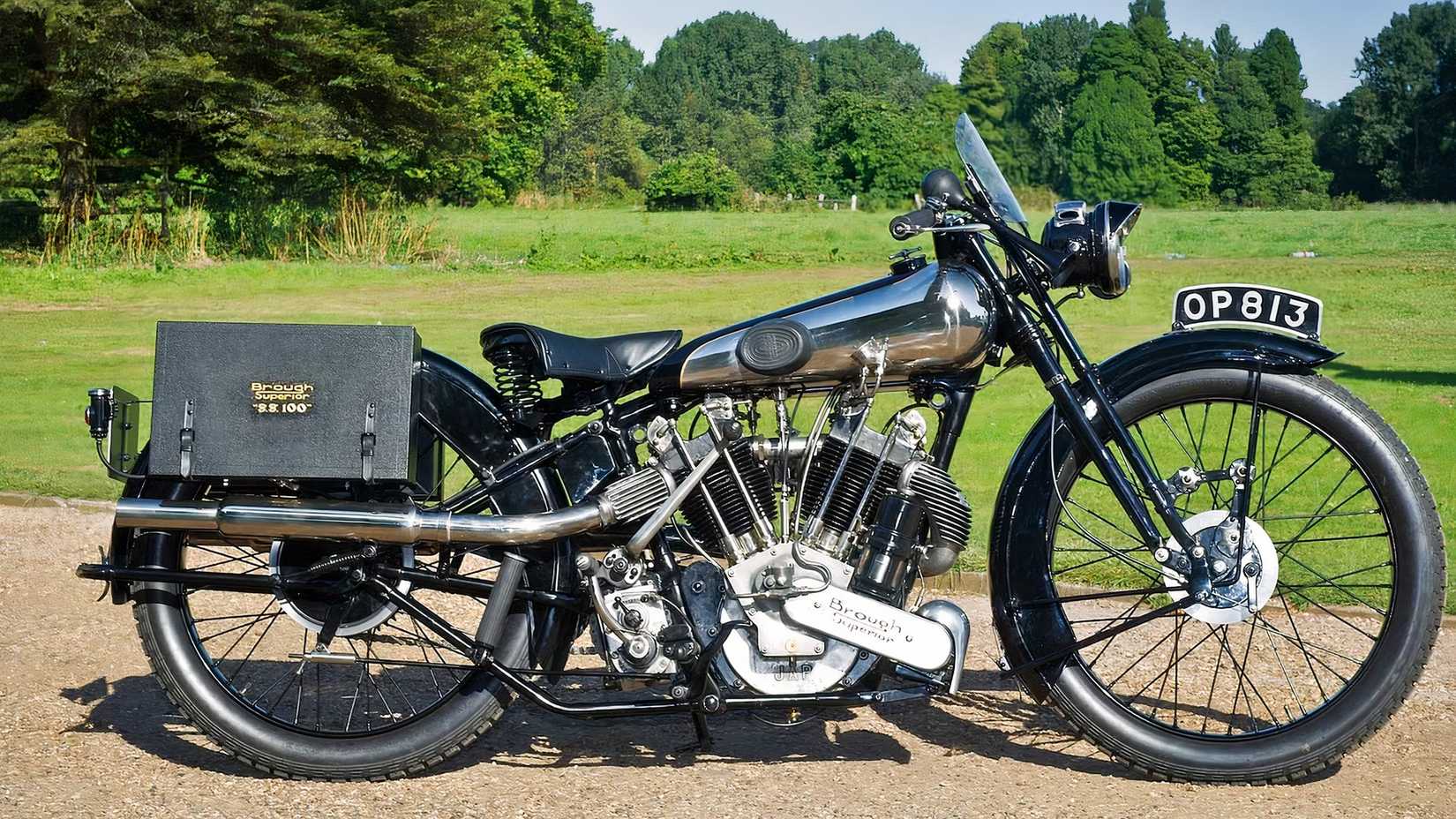Foto estática lateral do Brough Superior SS100 Alpine Sports em uma estrada de terra próxima a um campo