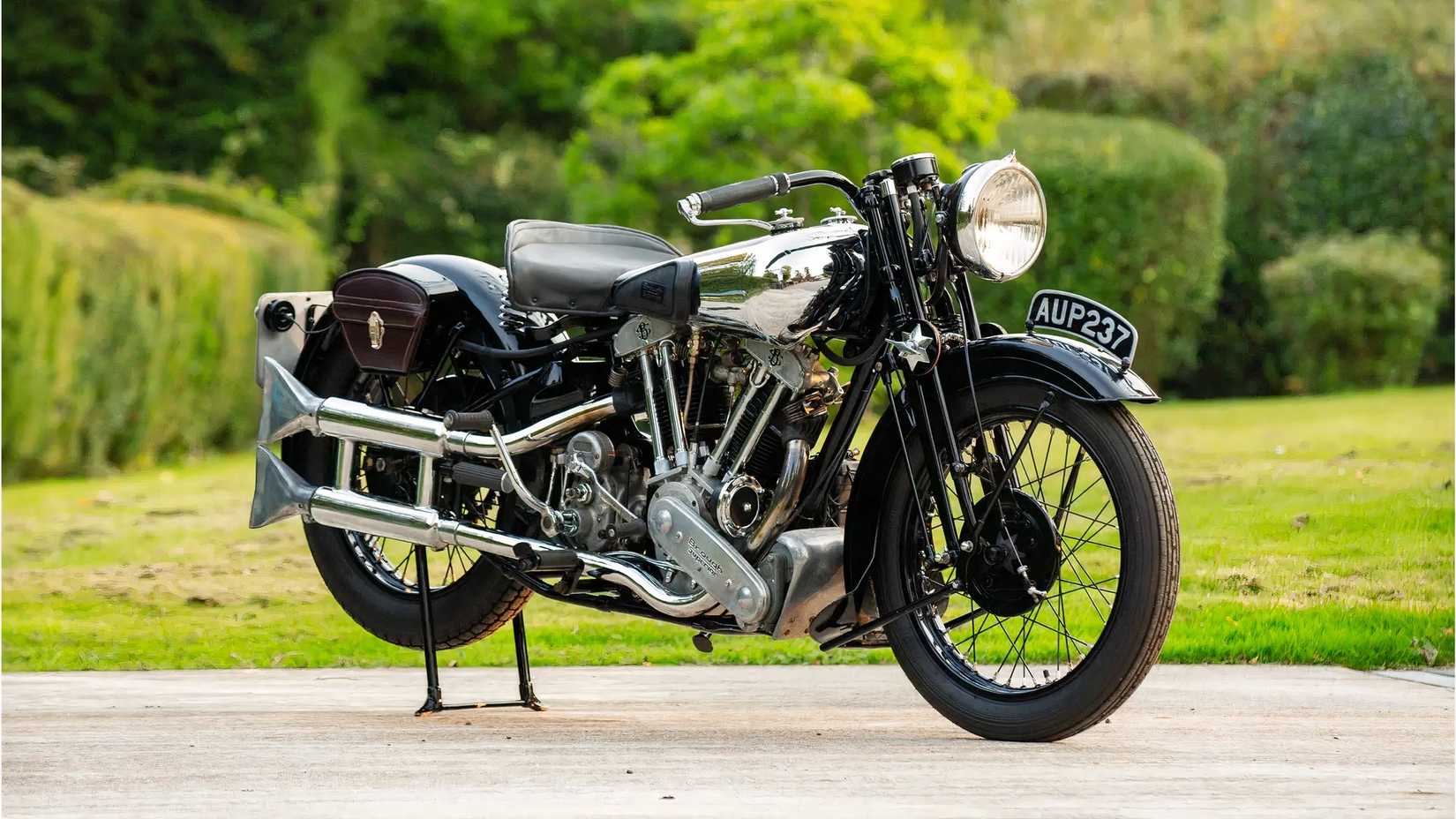 Foto estática de um Brough Superior SS100 1936 com motor Matchless estacionado em frente a um campo