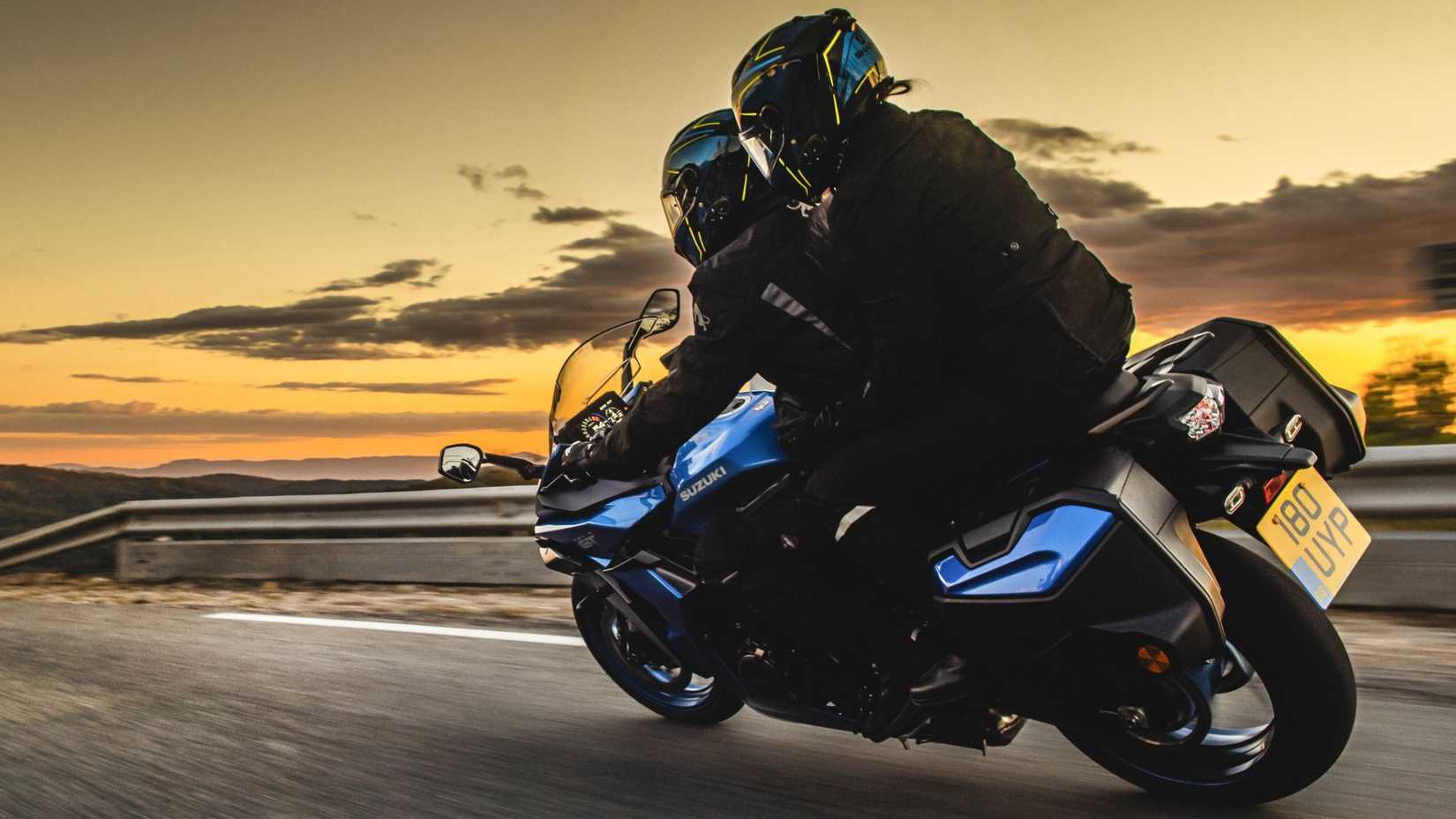 2026 Suzuki GSX-S1000GT+ cornering smoothly with a pillion and side cases cinematic rear third quarter view