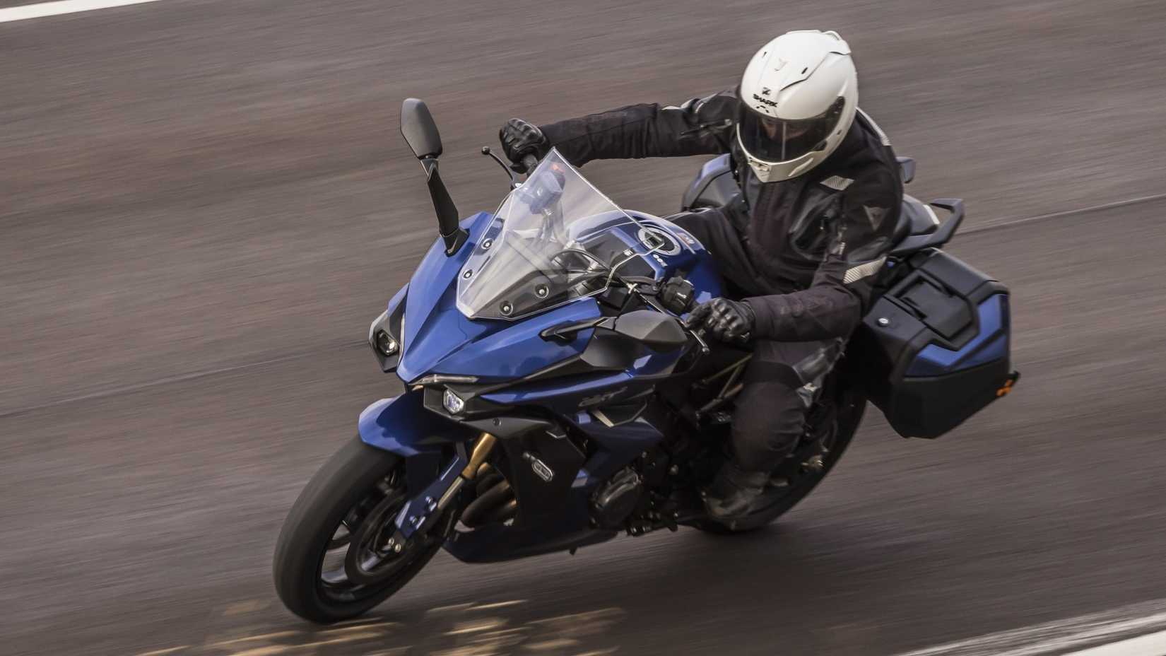 Suzuki GSX-S1000GT+ accelerating swiftly through a corner front third quarter ariel shot