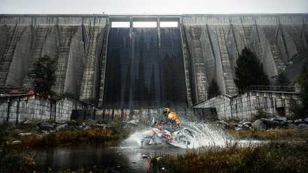 2025 KTM 390 Adventure R espirrando na água em frente a uma barragem