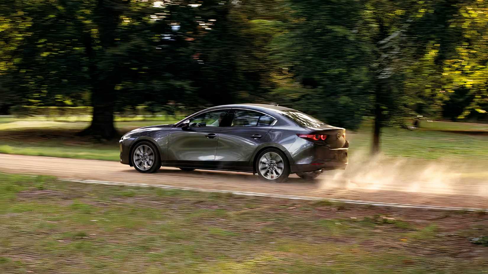 Foto de ação 3/4 traseira do Mazda 3 Sedan 2026 dirigindo em estrada de terra