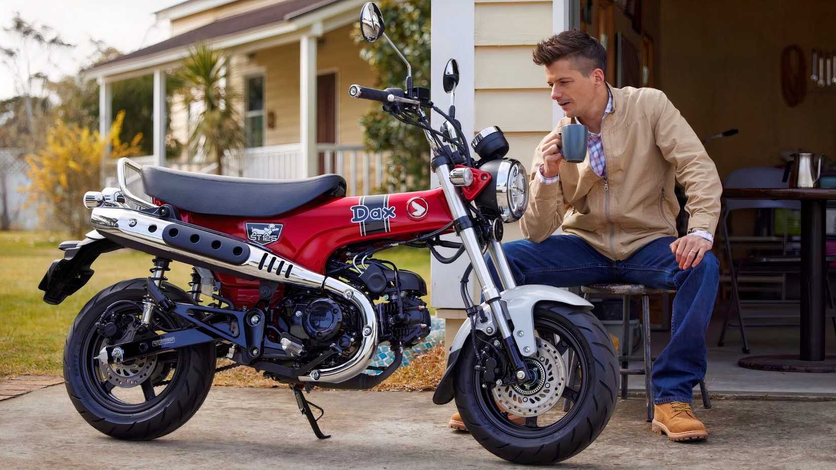 Uma foto estática da Honda DAX 125 com um piloto sentado ao lado