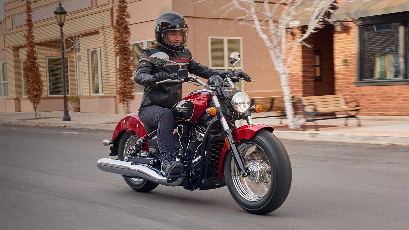 Piloto em um Indian Scout Classic vermelho 2026 cruzando a cidade