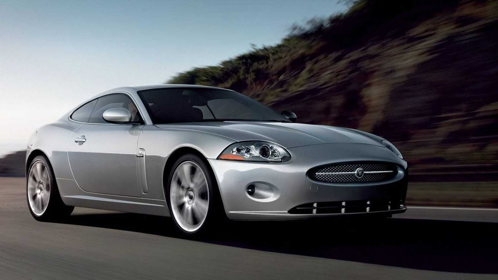 Uma cena de ação de um Jaguar XK pré-facelift cruzando uma estrada com muito vento