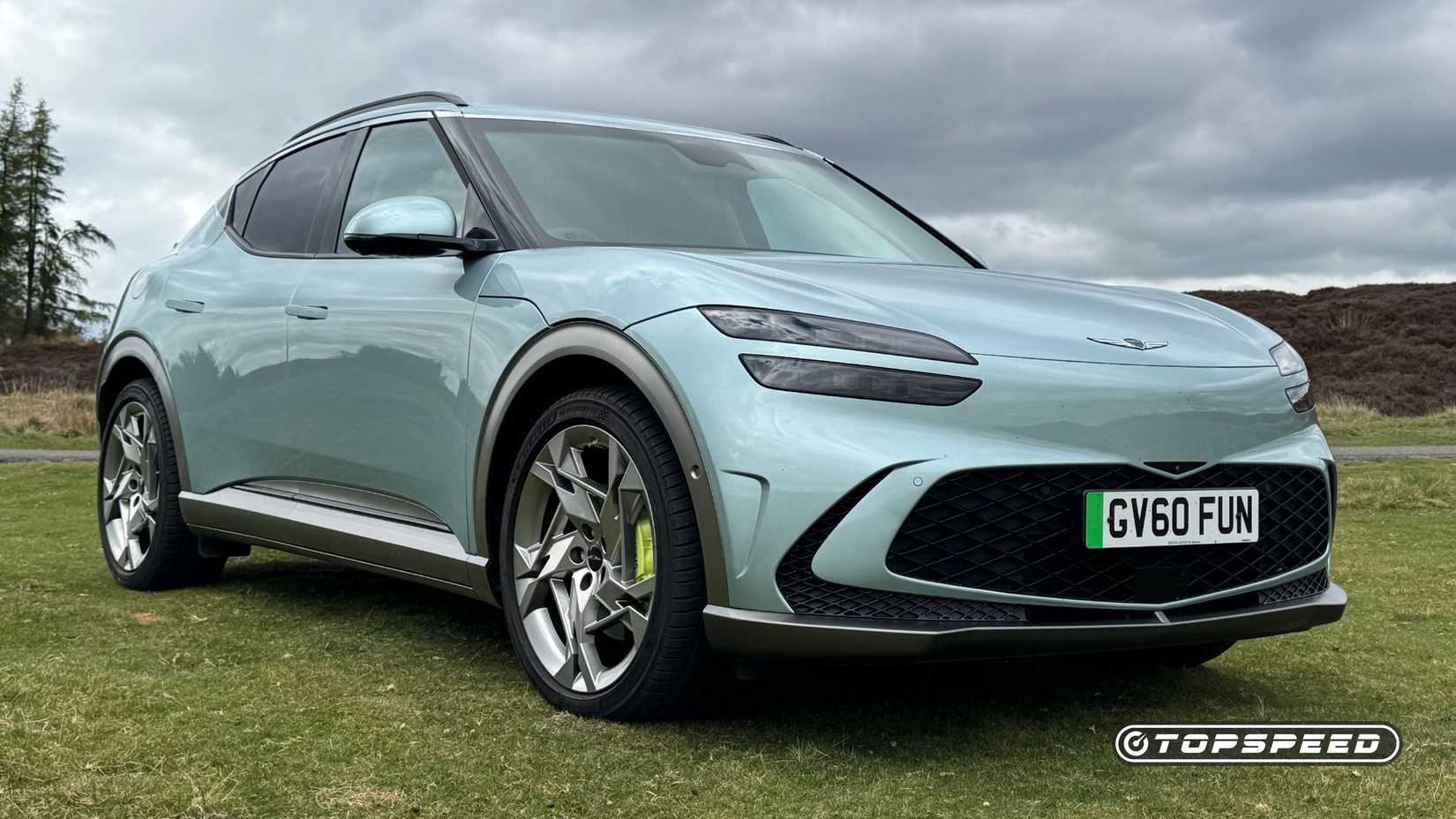 Static frotn 3/4 shot of a 2024 Genesis GV60 Sport Plus AWD parked on grass with trees in the background.