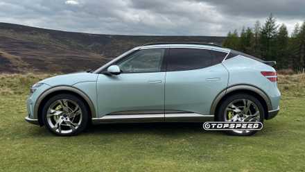 Static side profile shot of a 2024 Genesis GV60 Sport Plus AWD parked on grass with trees in the background.