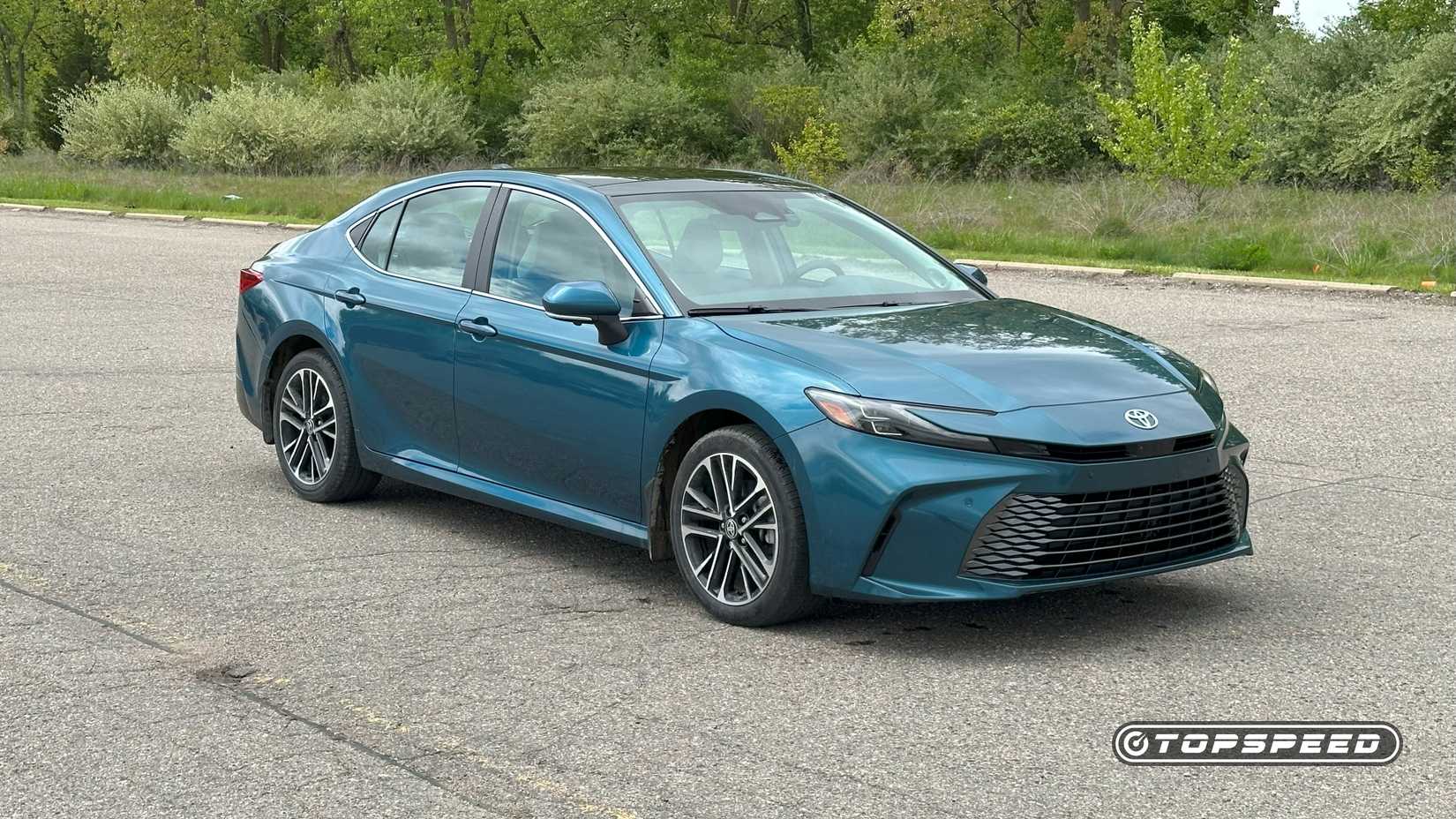 Front 3/4 shot of a blue 2025 Toyota Camry XLE AWD parked in front of trees
