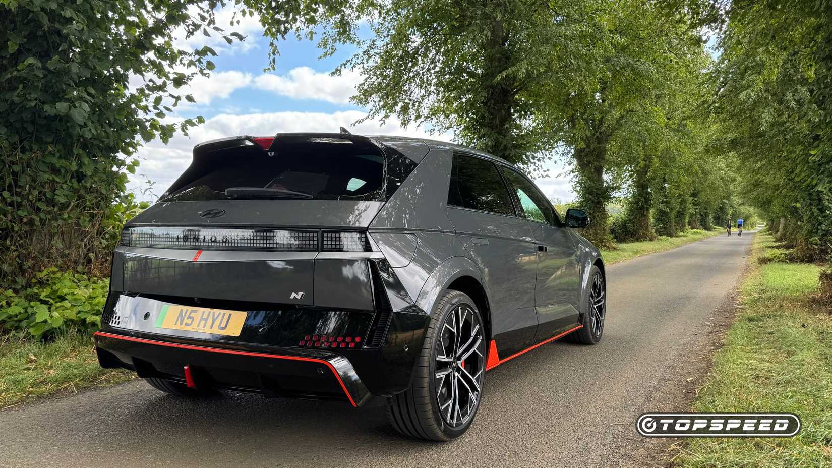 Static rear 3/4 shot of a gray 2025 Hyundai Ioniq 5 N parked on a country road lined by trees.